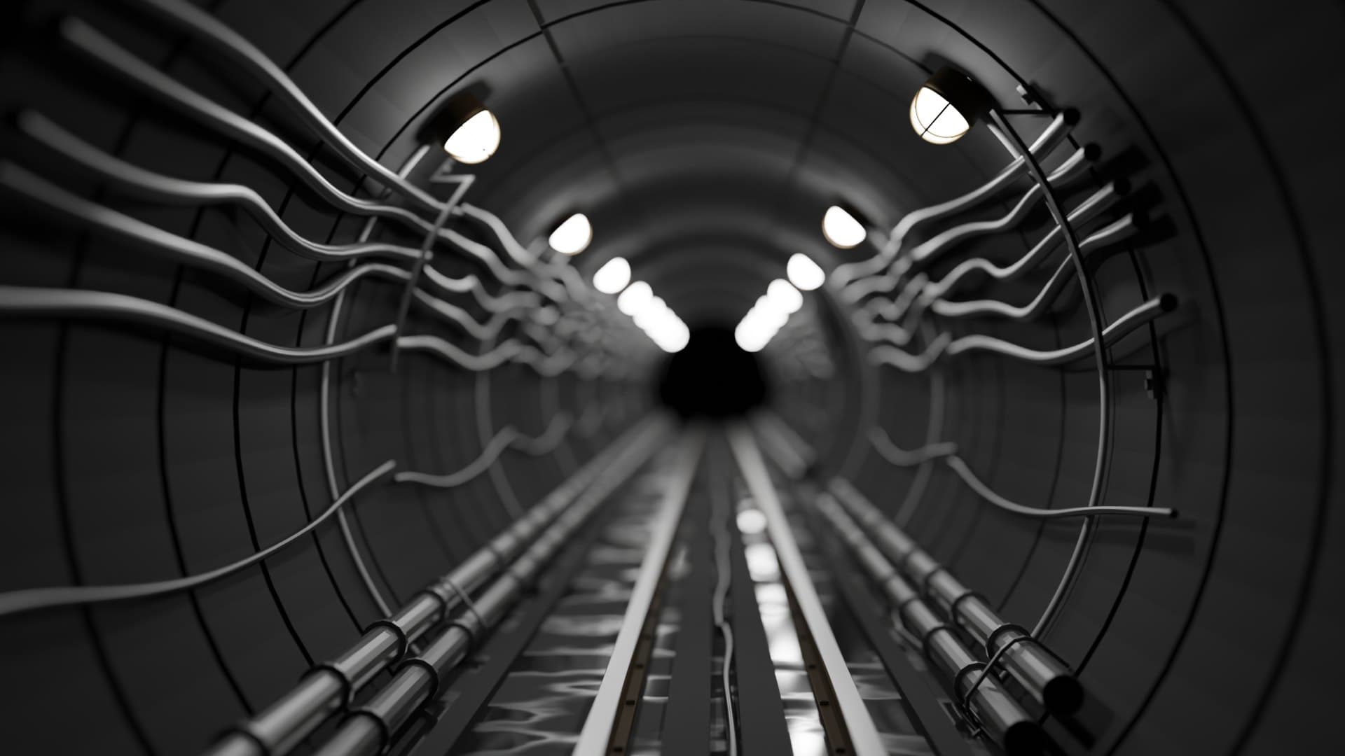 A black-and-white metro tunnel with cables along the walls and rails vanishing into the distance.