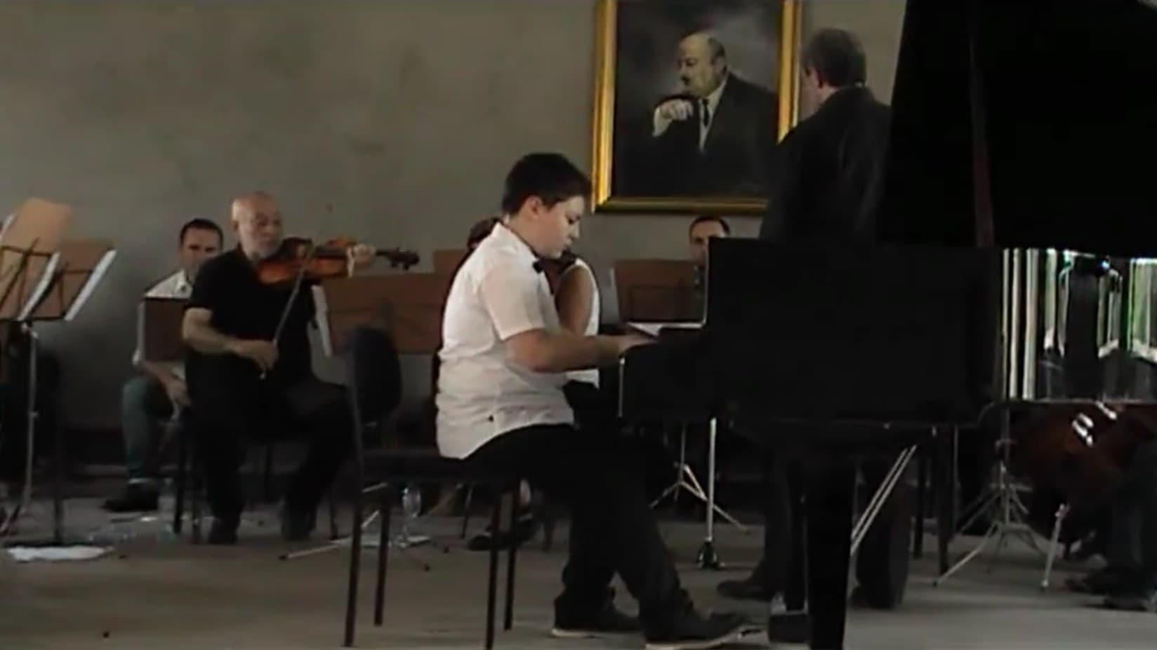 Aleksandre as a boy playing a grand piano, with string players behind him.