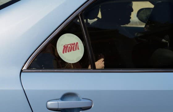 A pale blue car with a round Rashi sticker on its rear side window.
